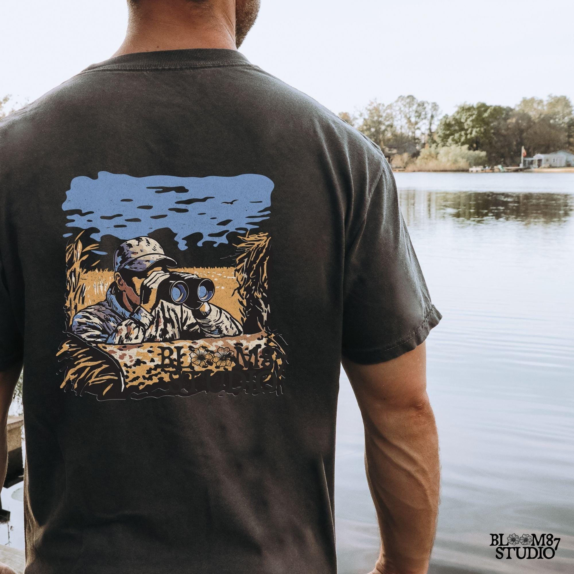 “Illustrated camouflage hunter peeking through binoculars from a duck blind, surrounded by tall grass, with a blue sky and golden field background. A detailed digital hunting-themed design, perfect for outdoorsmen, wildlife lovers, and hunting gear.”