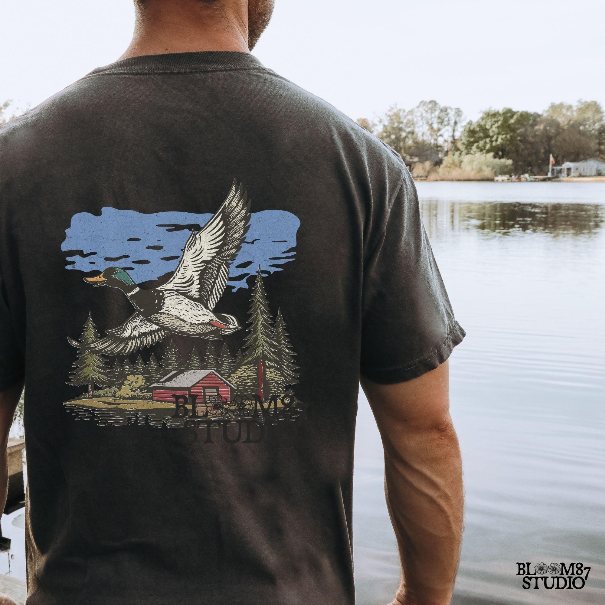 Vintage illustration of a mallard duck flying over a red cabin by the lake, surrounded by pine trees. Perfect for rustic lodge decor and wildlife art prints.