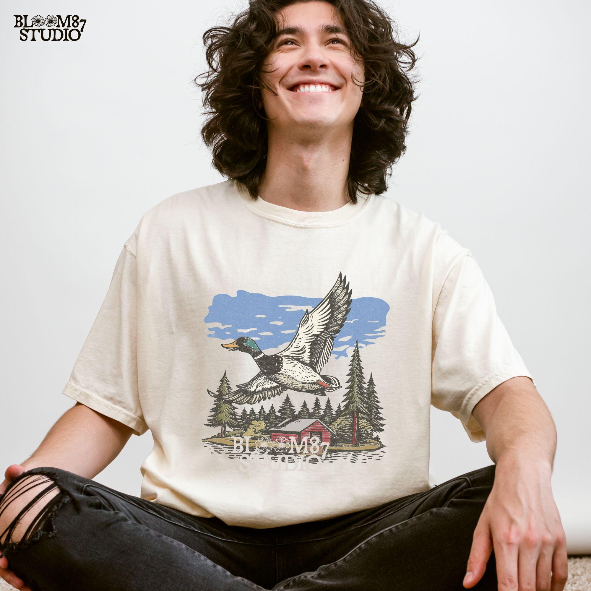 Vintage illustration of a mallard duck flying over a red cabin by the lake, surrounded by pine trees. Perfect for rustic lodge decor and wildlife art prints.