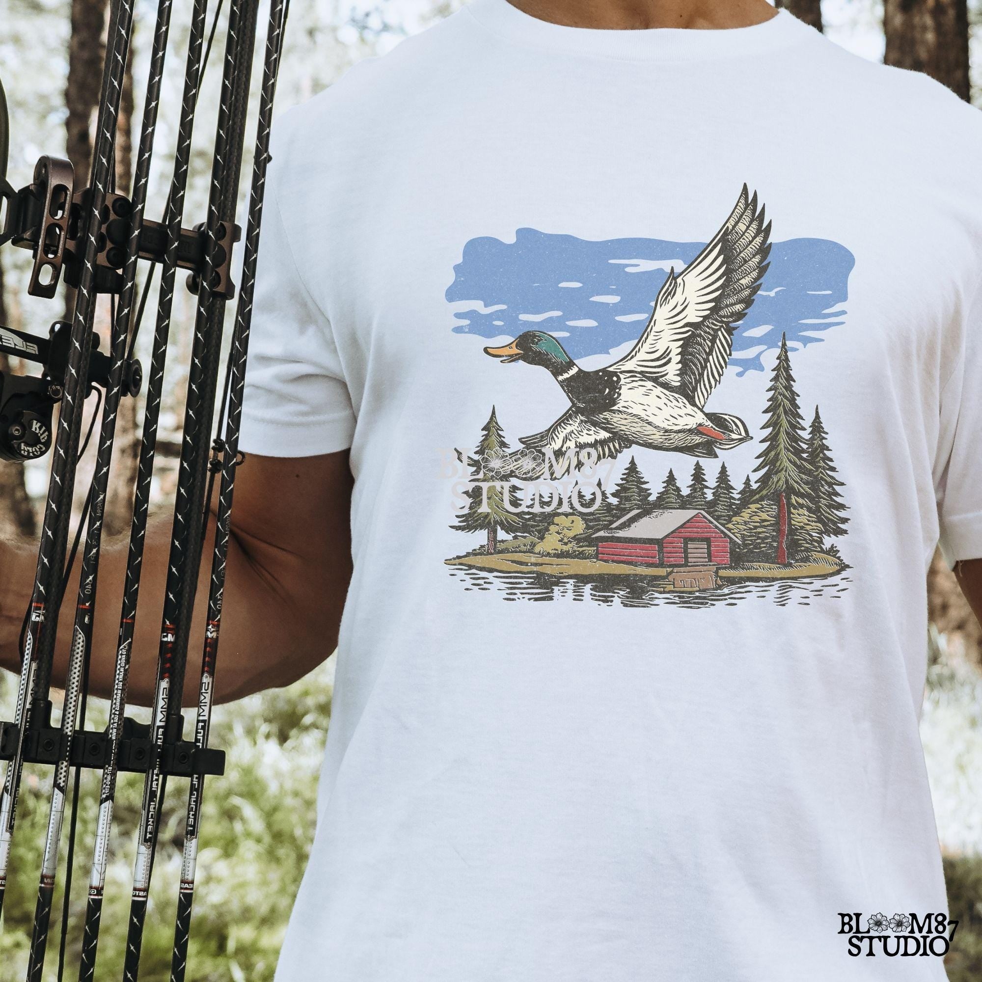 Vintage illustration of a mallard duck flying over a red cabin by the lake, surrounded by pine trees. Perfect for rustic lodge decor and wildlife art prints.