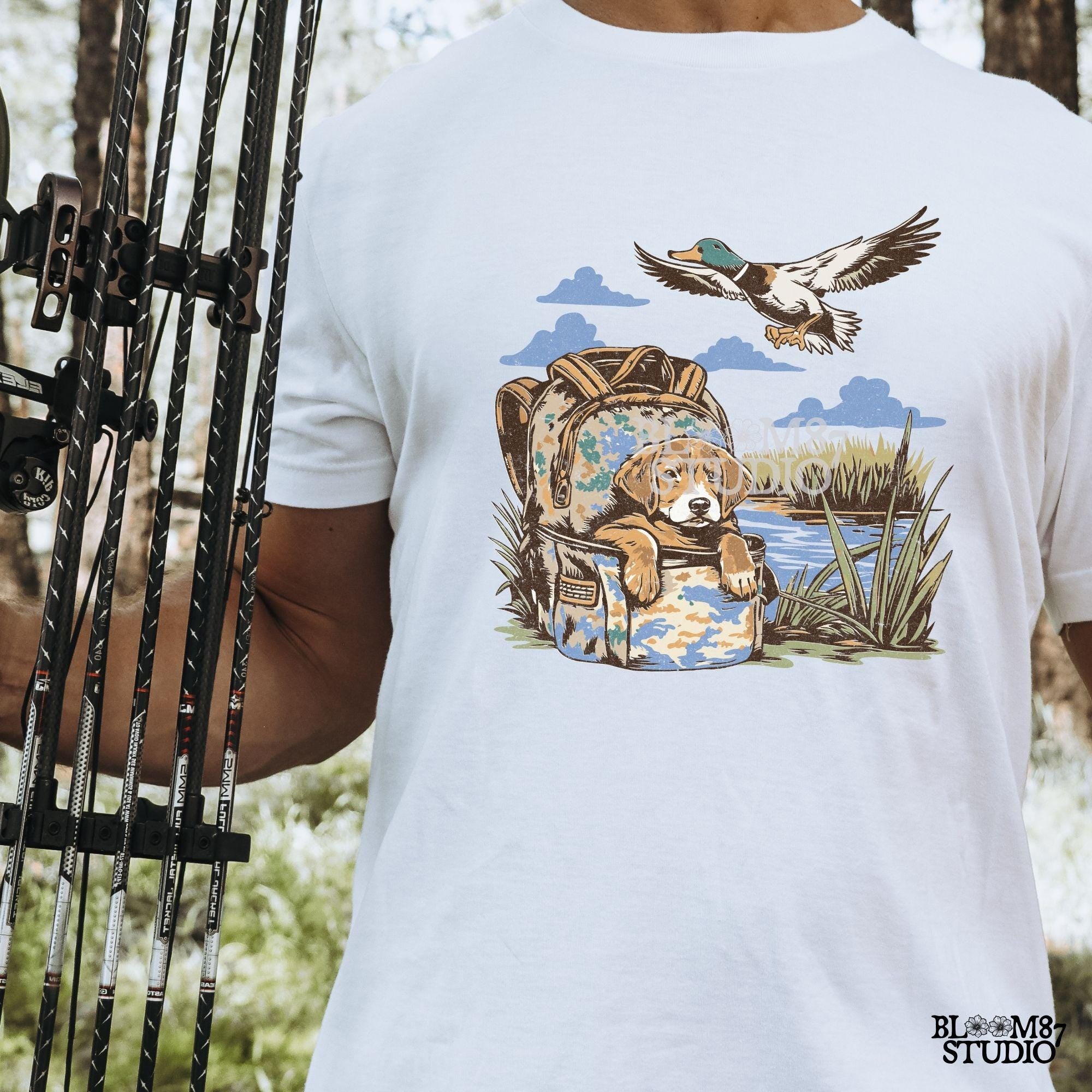 Illustration of a hunting dog resting in a camouflage bag near a pond, with a mallard duck flying overhead in a peaceful outdoor setting.