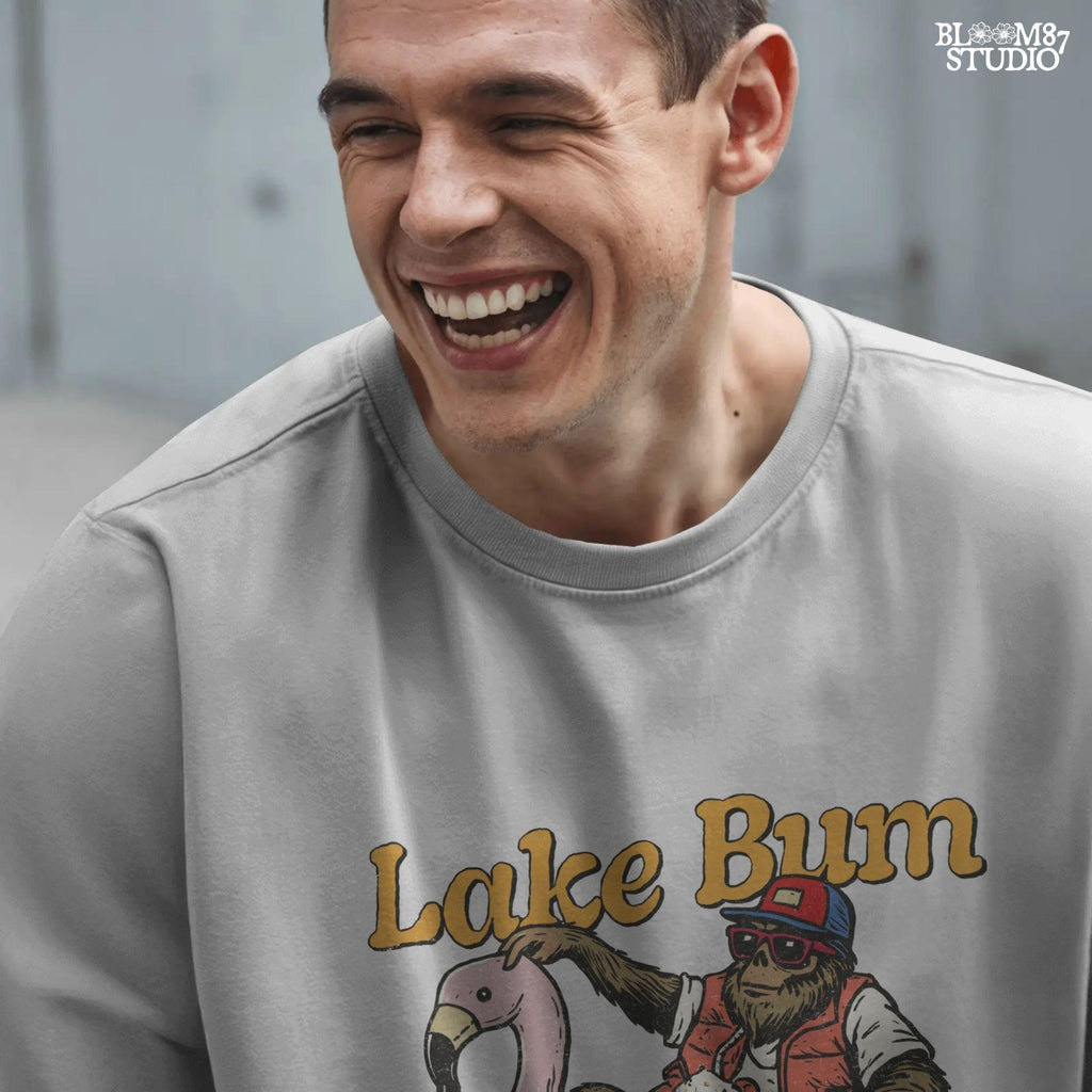 Bigfoot lounging on a pink flamingo float with a beer, wearing summer gear and sunglasses, with “Lake Bum” text above.