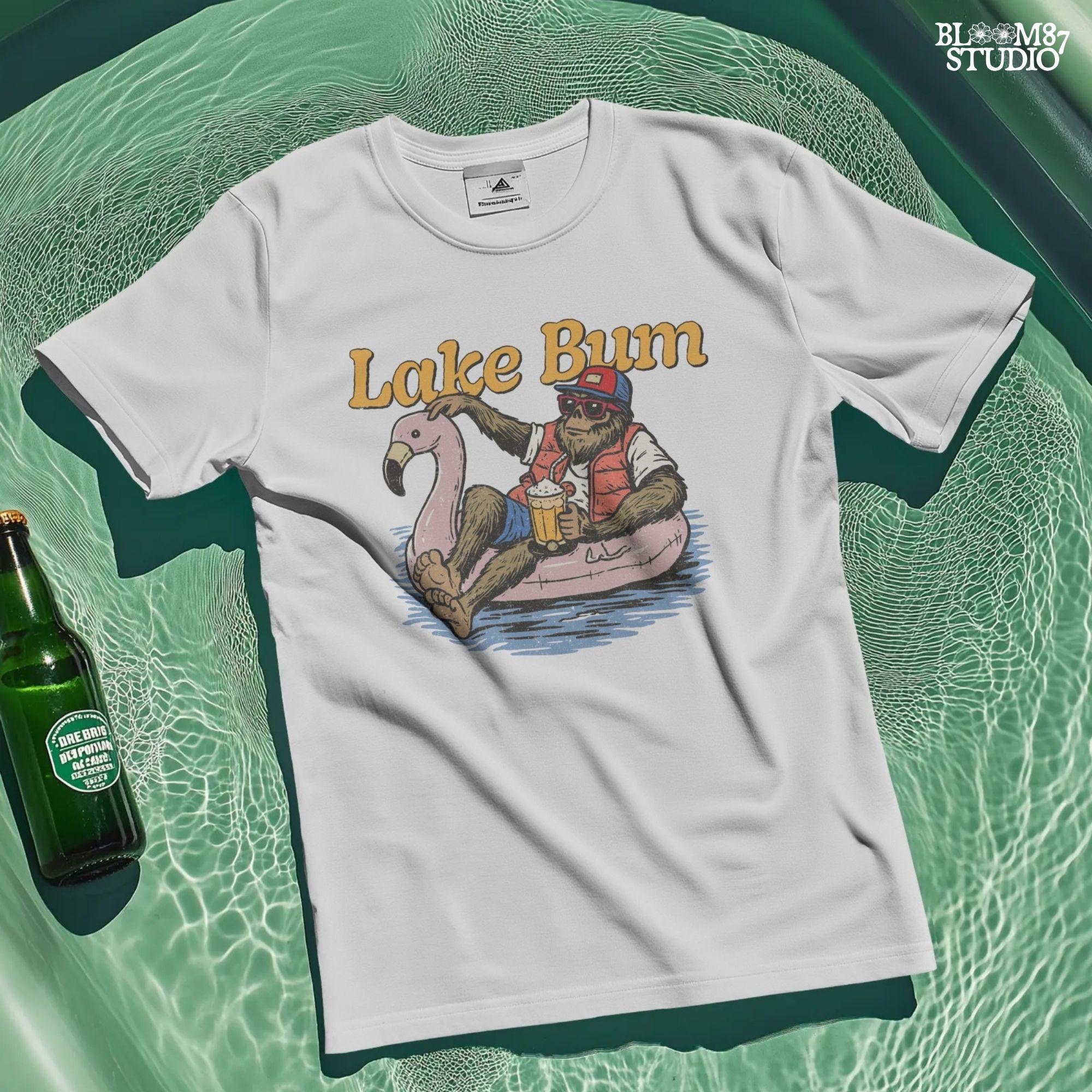 Bigfoot lounging on a pink flamingo float with a beer, wearing summer gear and sunglasses, with “Lake Bum” text above.