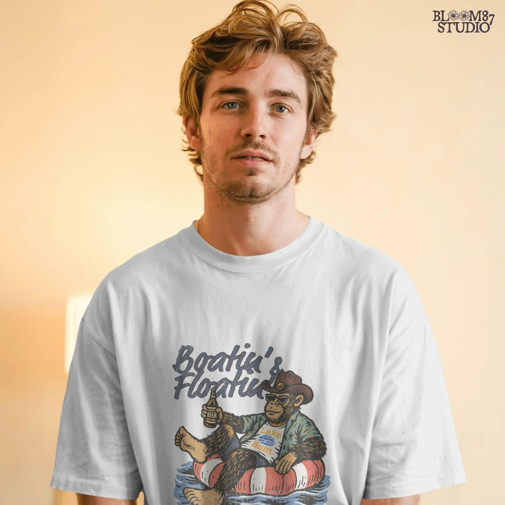 Bigfoot relaxing in a red and white pool float, holding a beer and wearing sunglasses, a hat, and a tropical shirt with “Boatin’ & Floatin’” text above.