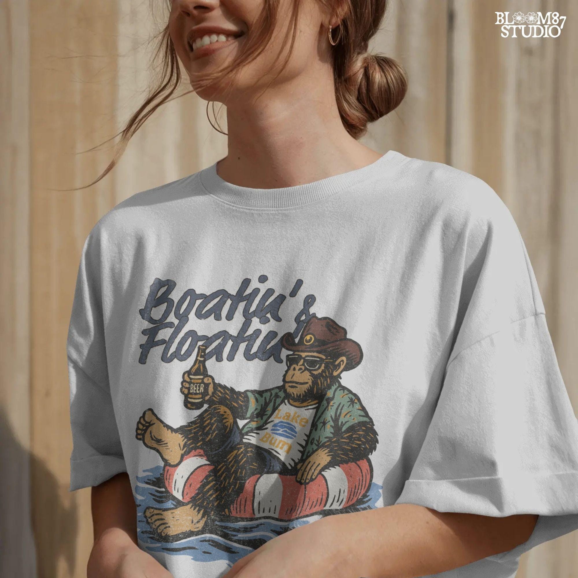 Bigfoot relaxing in a red and white pool float, holding a beer and wearing sunglasses, a hat, and a tropical shirt with “Boatin’ & Floatin’” text above.