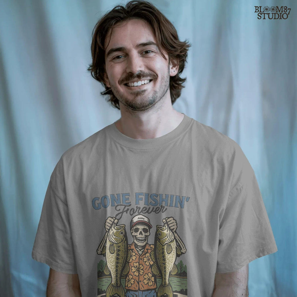 A skeleton wearing a red cap and orange floral shirt stands on a dock holding two large bass fish with the words “Gone Fishin’ Forever” above.