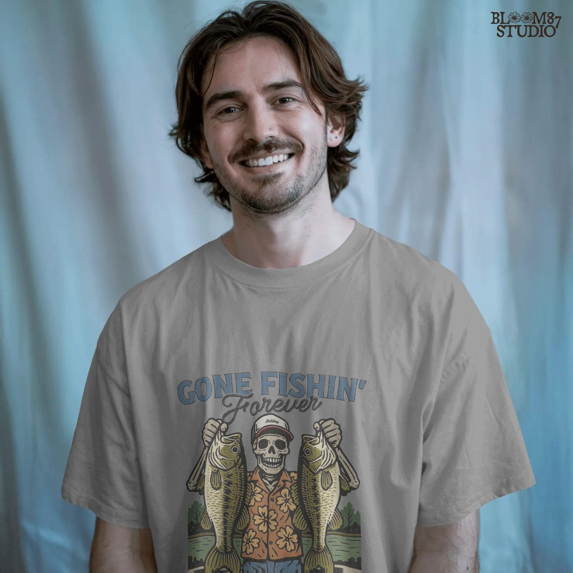 A skeleton wearing a red cap and orange floral shirt stands on a dock holding two large bass fish with the words “Gone Fishin’ Forever” above.