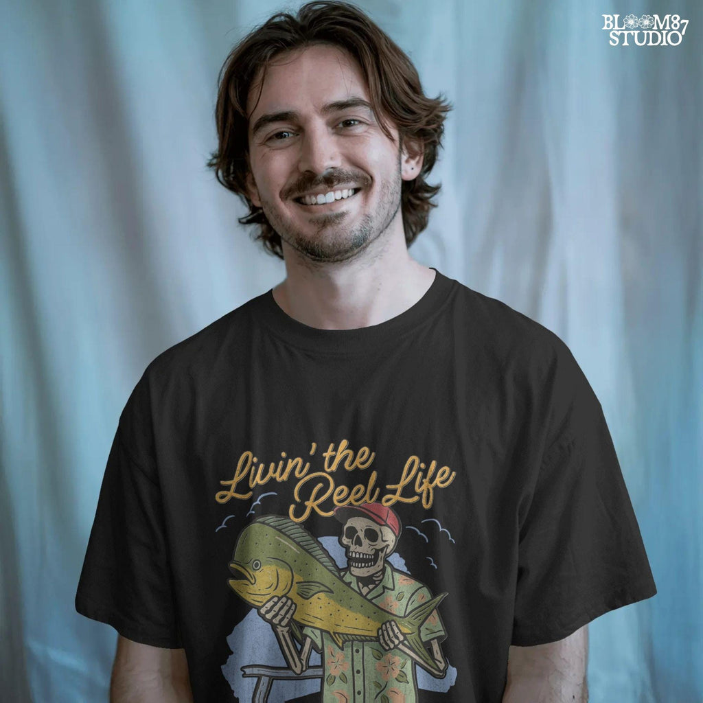 Cartoon skeleton in tropical shirt holding a mahi-mahi fish with text “Livin’ the Reel Life” above and “Hooked & Happy Co.” below.