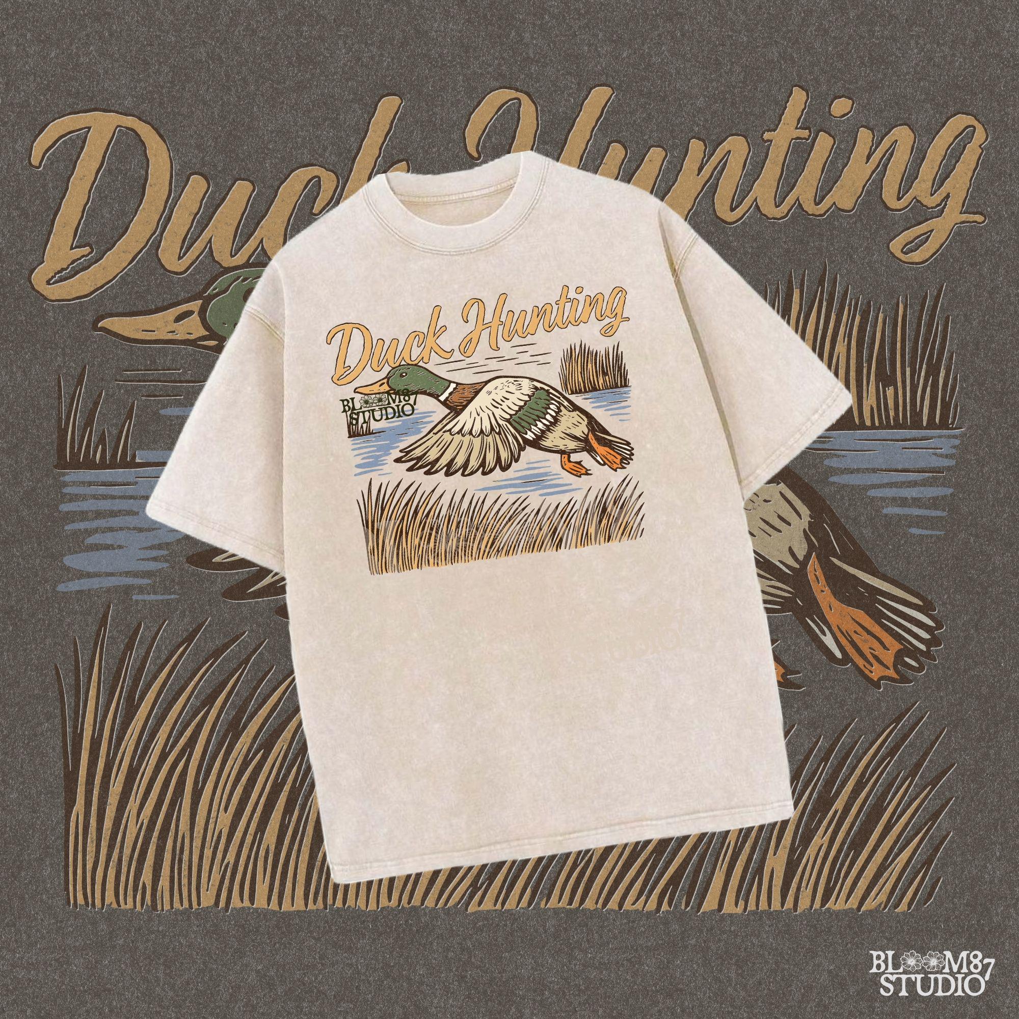 Vintage woodcut-style illustration of a mallard duck flying over marshy water with tall reeds and “Duck Hunting” text in bold script.