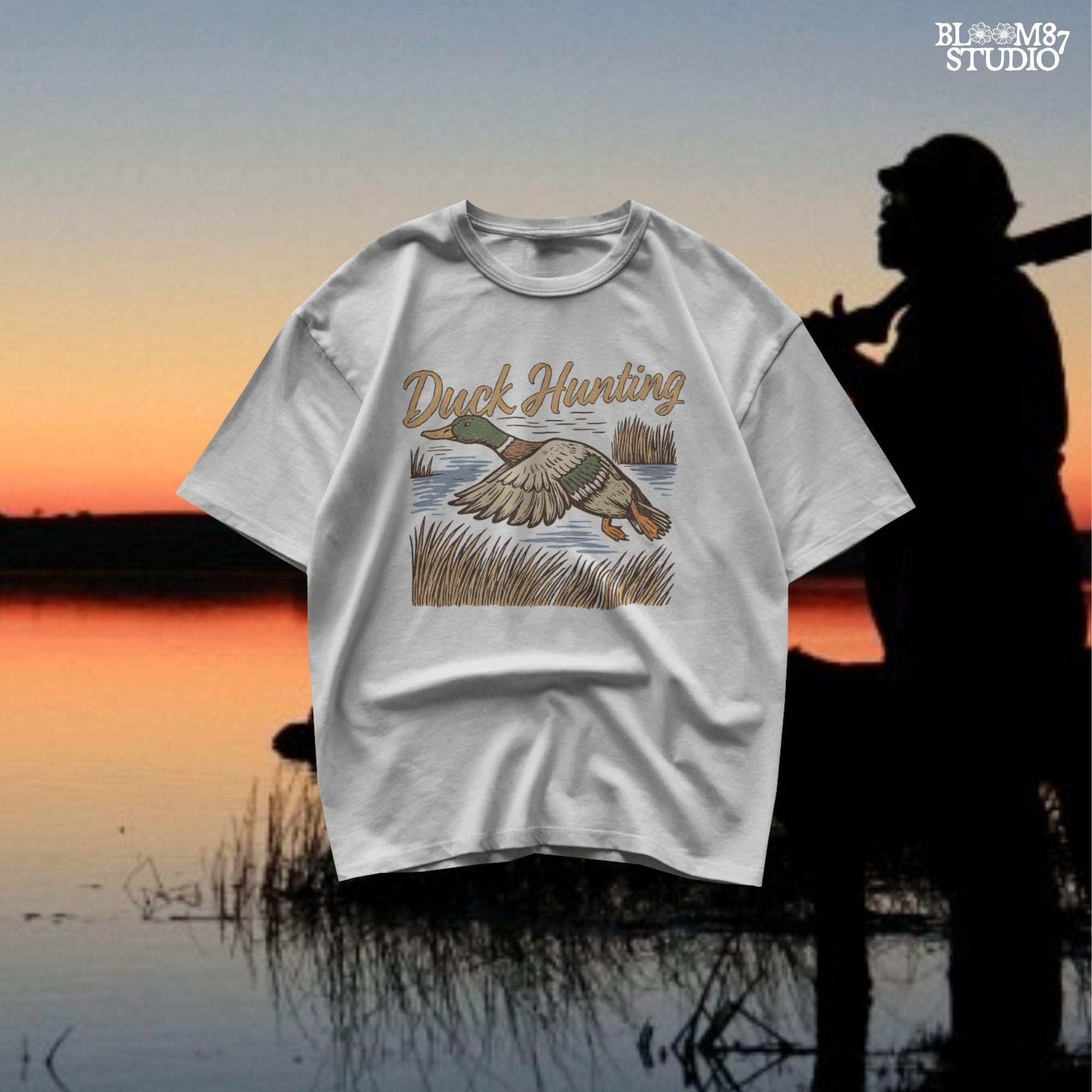 Vintage woodcut-style illustration of a mallard duck flying over marshy water with tall reeds and “Duck Hunting” text in bold script.