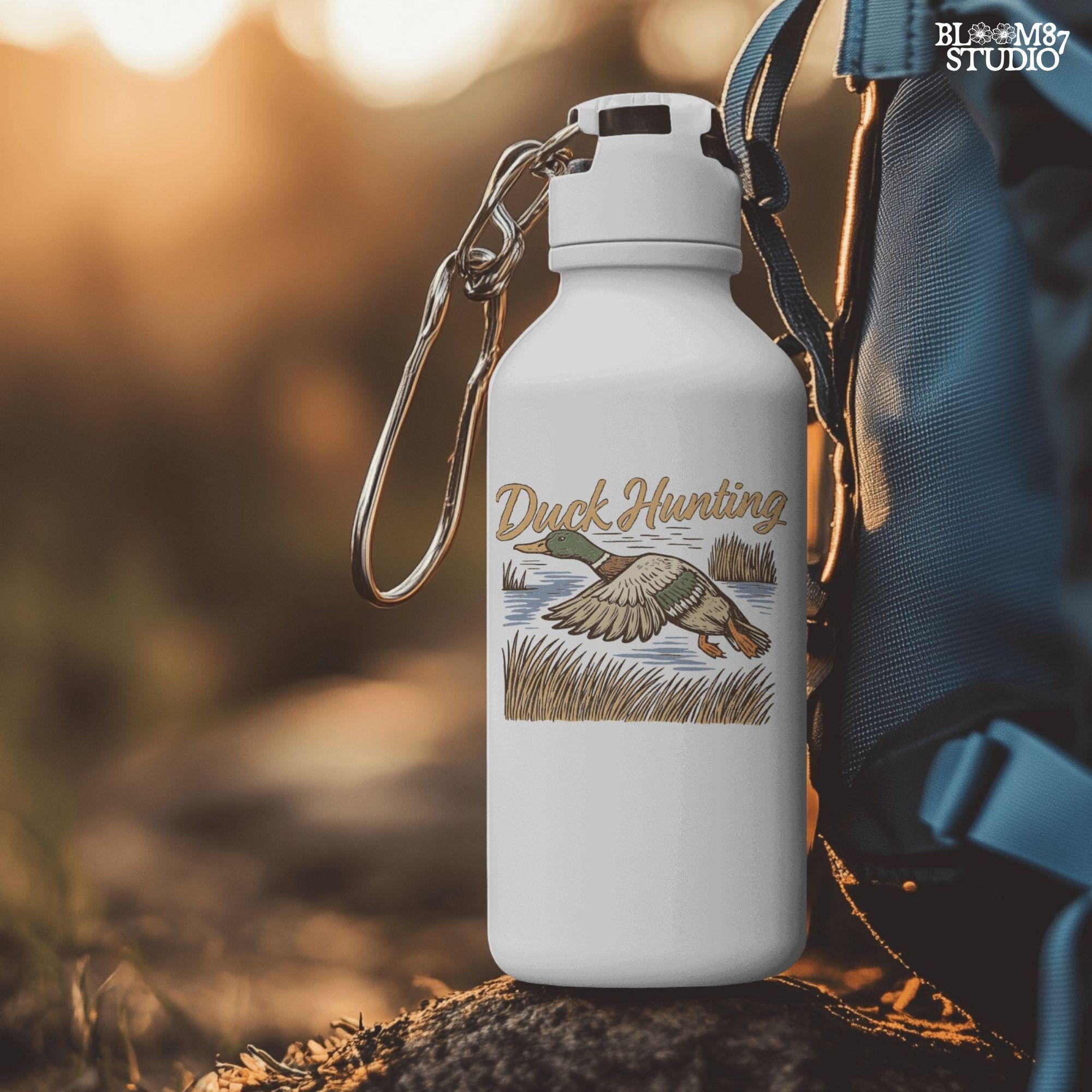 Vintage woodcut-style illustration of a mallard duck flying over marshy water with tall reeds and “Duck Hunting” text in bold script.