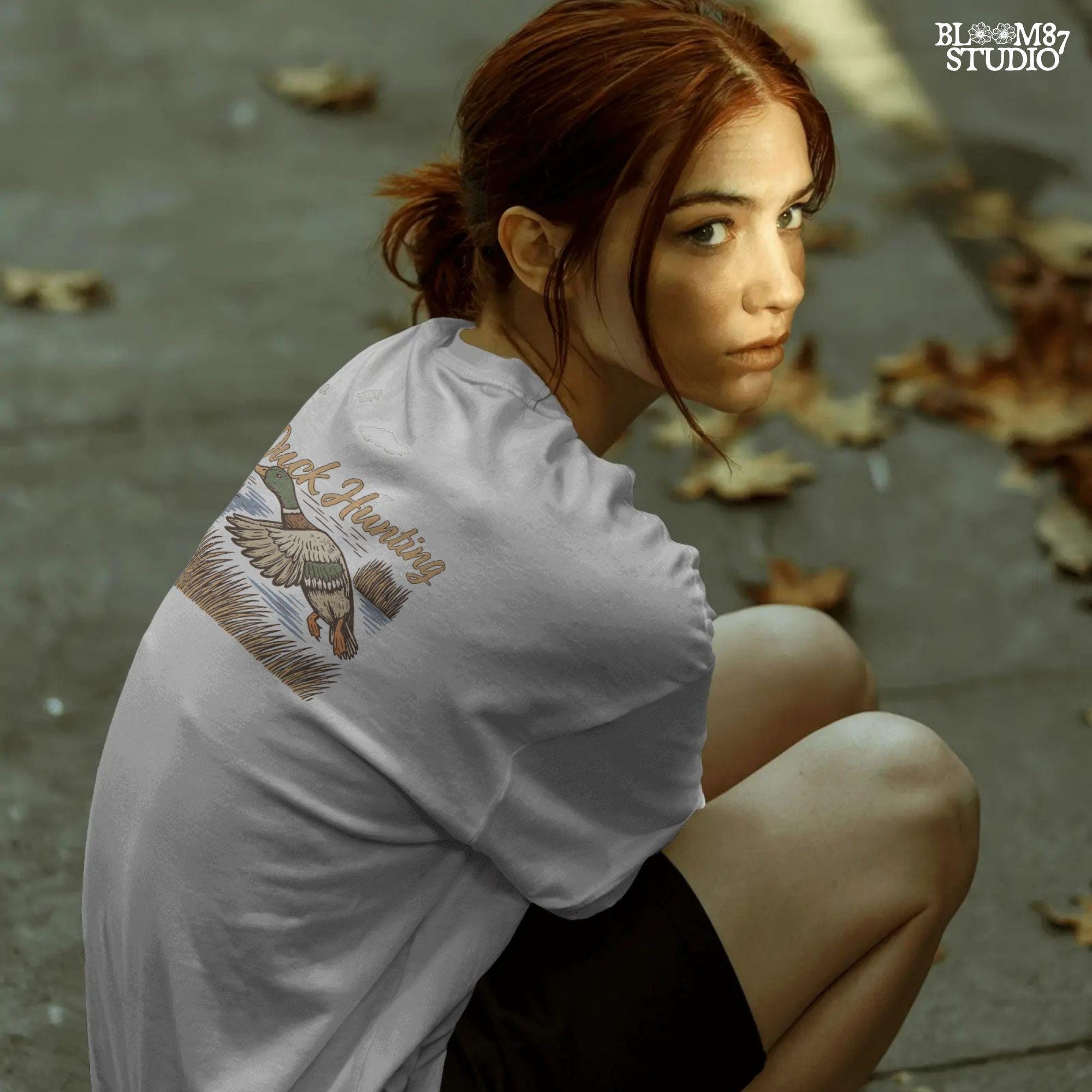 Vintage woodcut-style illustration of a mallard duck flying over marshy water with tall reeds and “Duck Hunting” text in bold script.