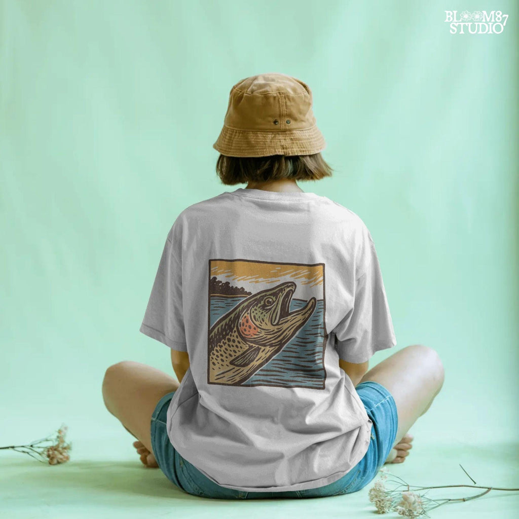 Vintage woodcut-style illustration of a trout fish leaping from the water at sunset, with a bold orange sky and retro color palette.