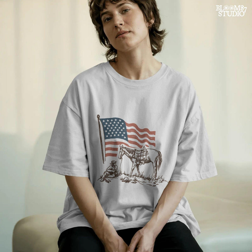 Vintage-style illustration of a cowboy sitting beside a saddled horse under a waving American flag.