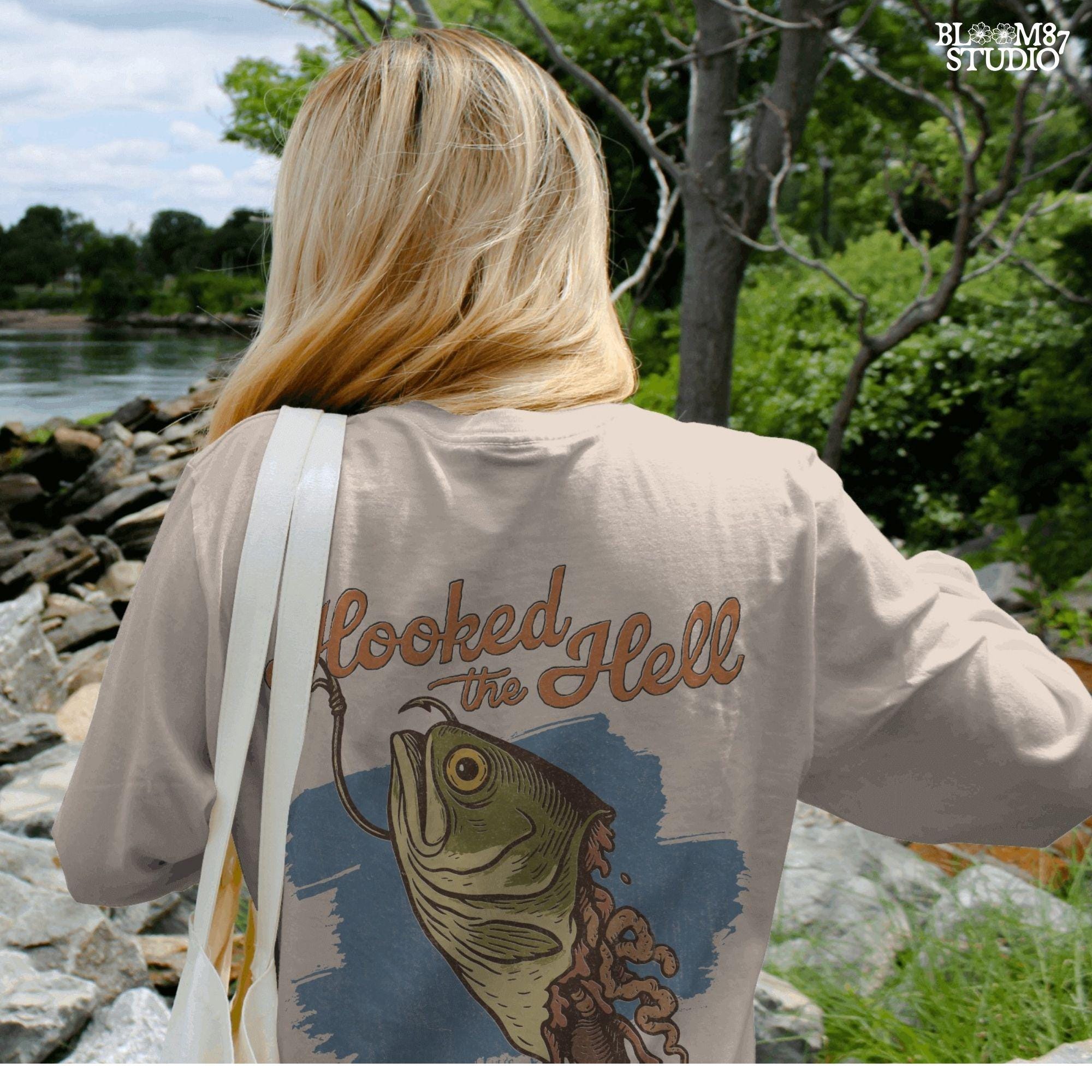 Funny exaggerated bass fish graphic with a hook through its mouth and dramatic detailing, paired with the text “Hooked the Hell” and “Bass Ain’t Gettin Back.”