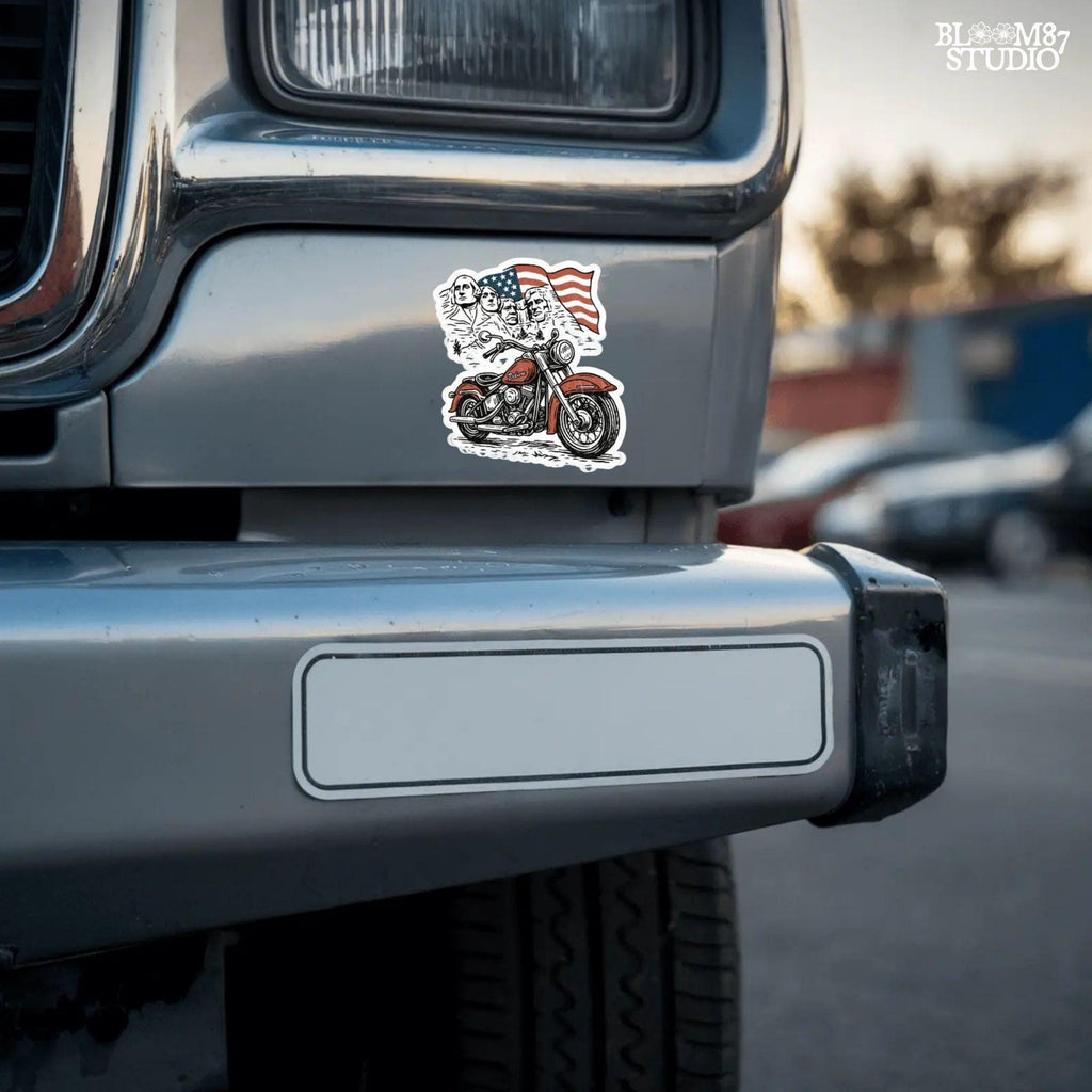 Vintage motorcycle graphic in front of Mount Rushmore and a waving American flag, styled in patriotic colors with retro biker design elements.