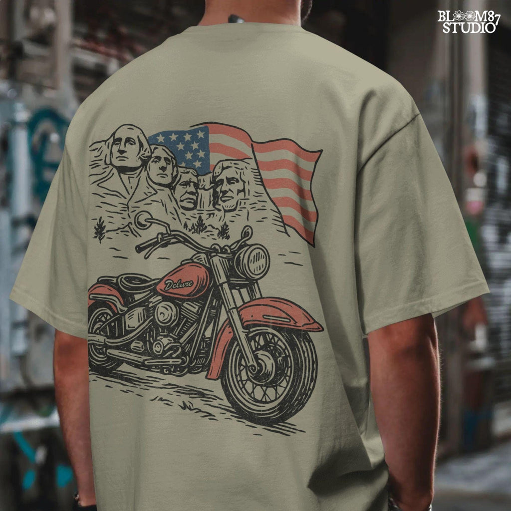 Vintage motorcycle graphic in front of Mount Rushmore and a waving American flag, styled in patriotic colors with retro biker design elements.