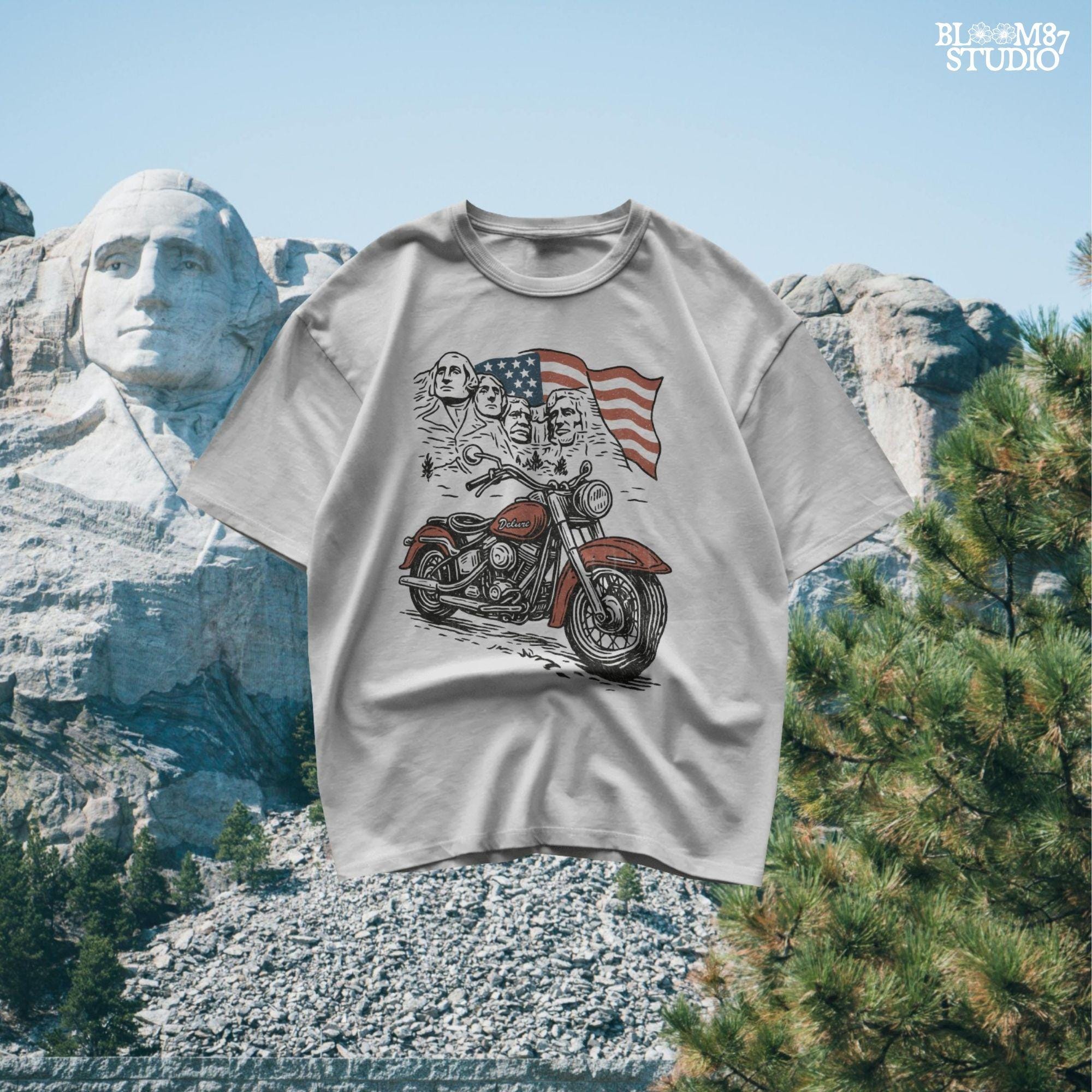 Vintage motorcycle graphic in front of Mount Rushmore and a waving American flag, styled in patriotic colors with retro biker design elements.
