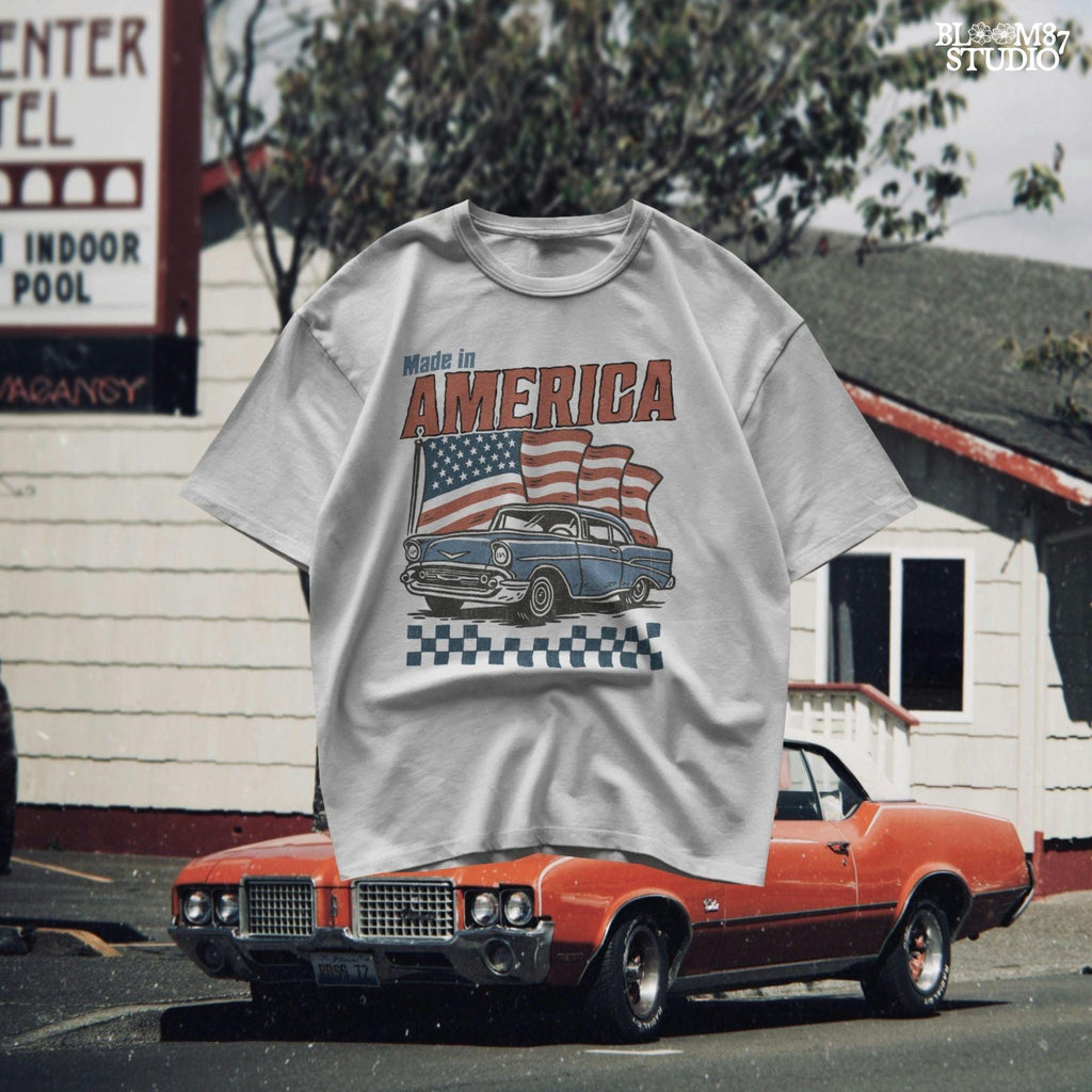 Classic American vintage car driving in front of three waving USA flags with “Made in America” text in bold retro style.
