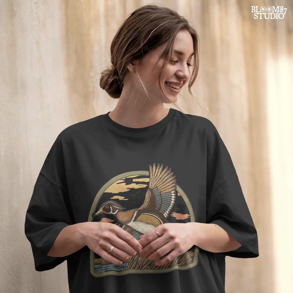 Illustration of a wood duck flying above a marsh at sunset with warm-toned clouds, cattails, and a reflective waterline.