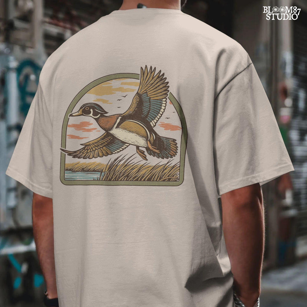 Illustration of a wood duck flying above a marsh at sunset with warm-toned clouds, cattails, and a reflective waterline.