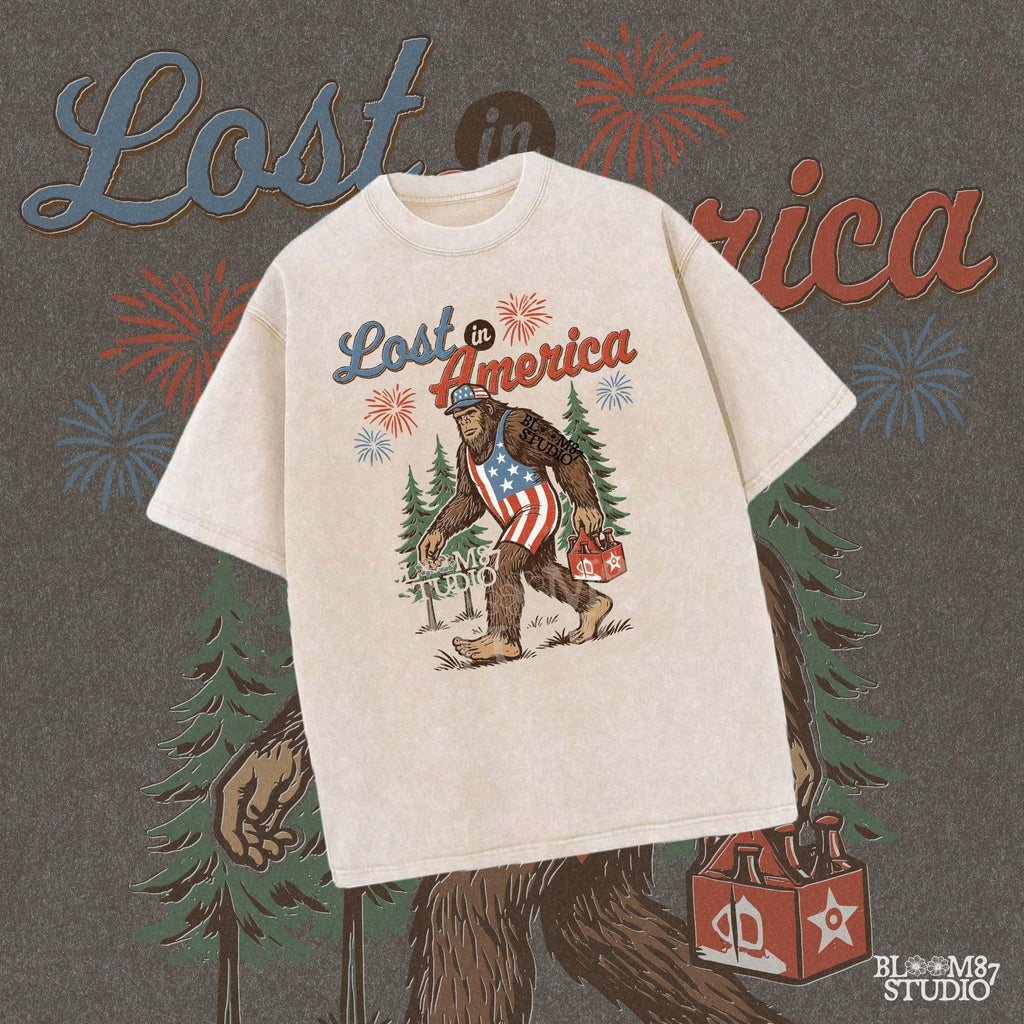 Bigfoot wearing an American flag outfit, carrying a six-pack of beer, walking through pine trees with fireworks in the sky and the phrase “Lost in America.”