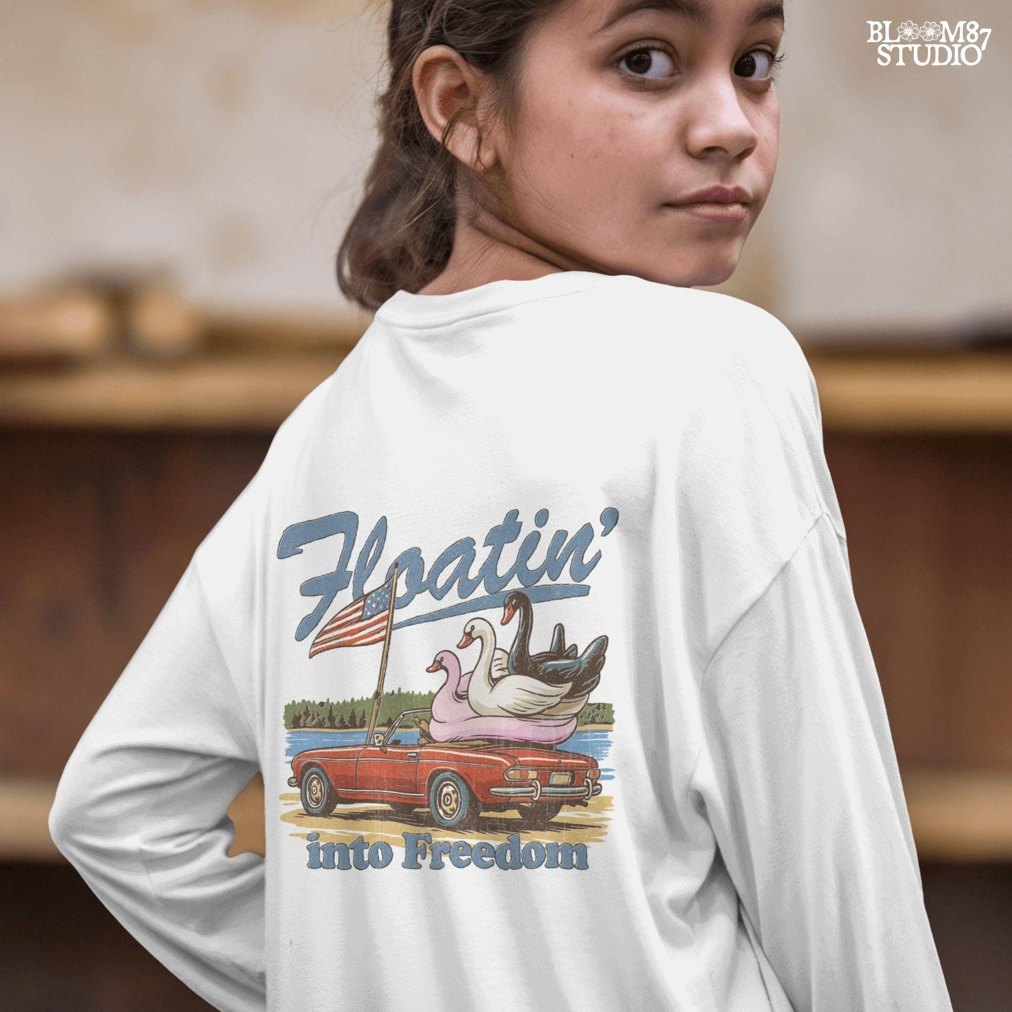 A red convertible car on the beach carrying three swan pool floats with an American flag, with the text “Floatin’ into Freedom” in a playful patriotic theme.
