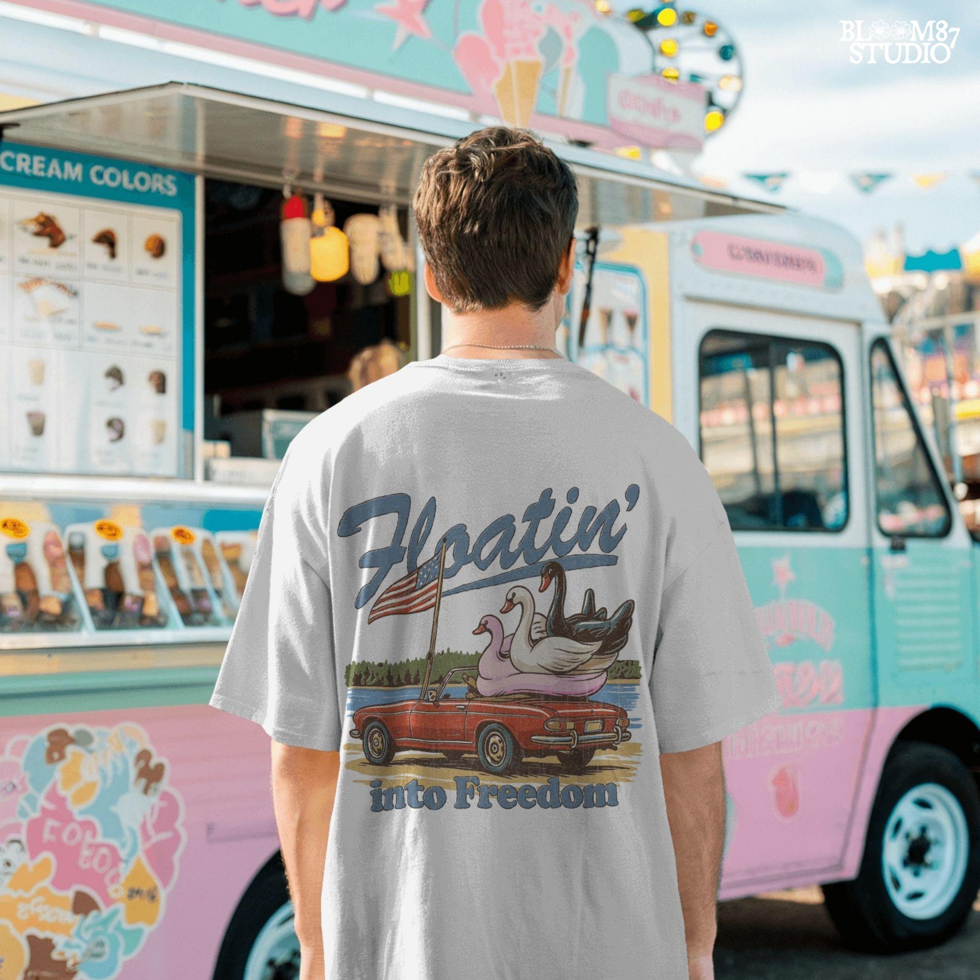 A red convertible car on the beach carrying three swan pool floats with an American flag, with the text “Floatin’ into Freedom” in a playful patriotic theme.