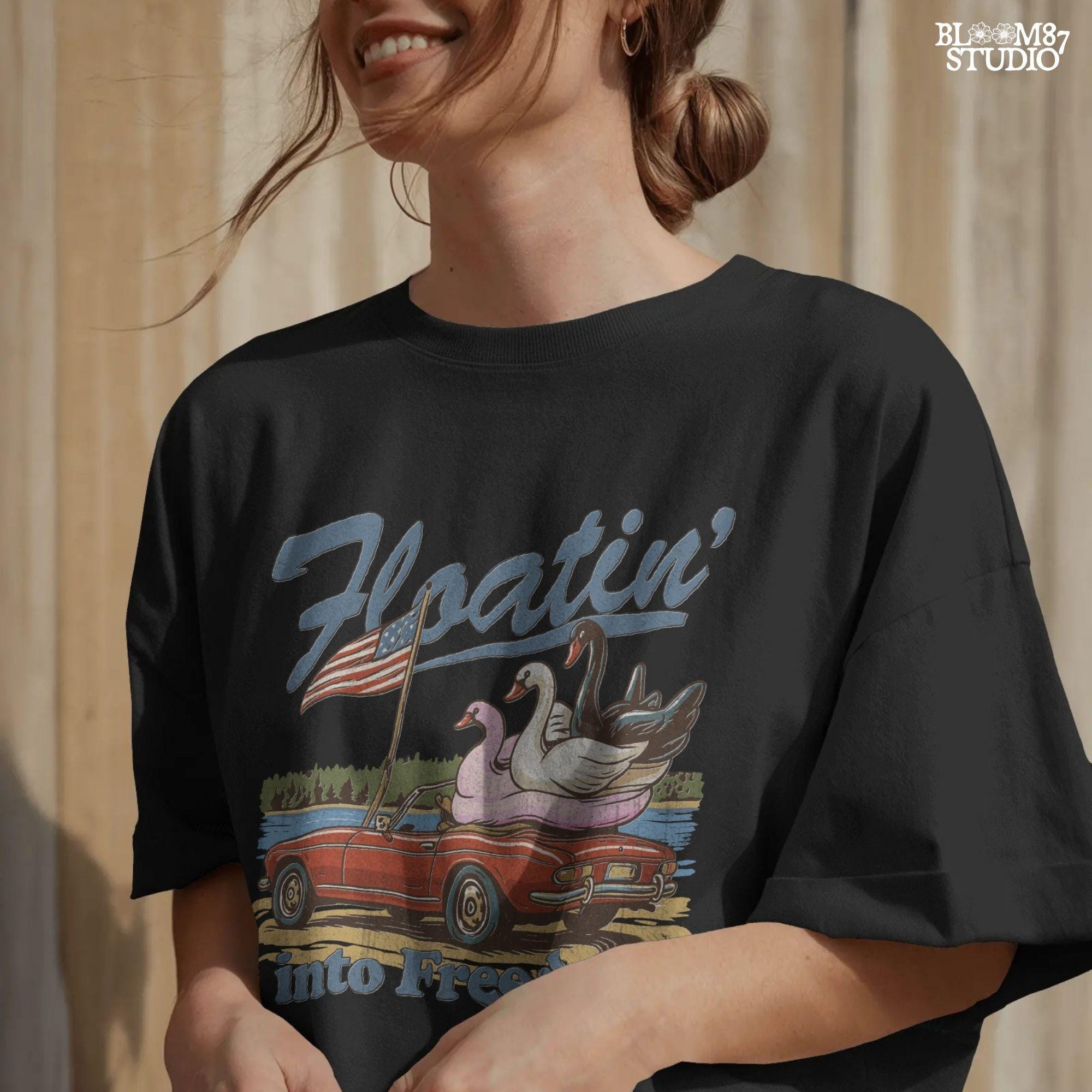 A red convertible car on the beach carrying three swan pool floats with an American flag, with the text “Floatin’ into Freedom” in a playful patriotic theme.