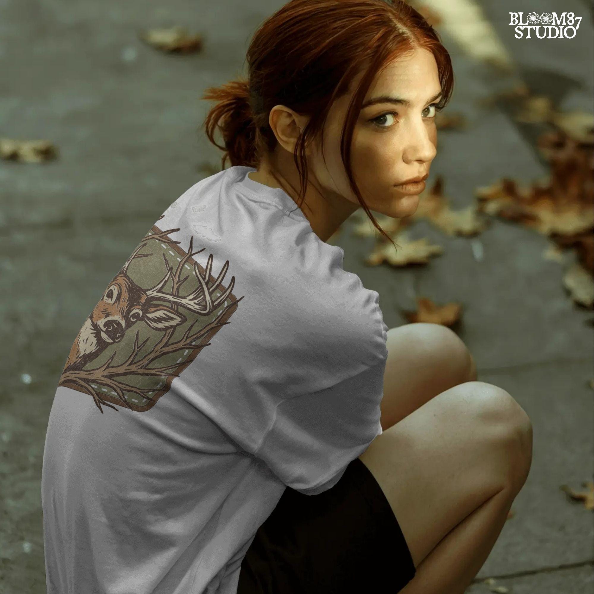 Stylized deer head with antlers framed by bare branches, placed on an olive green patch background with stitching detail.