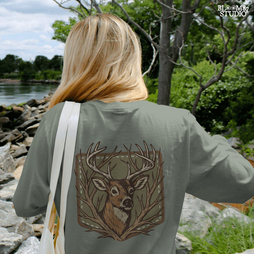 Stylized deer head with antlers framed by bare branches, placed on an olive green patch background with stitching detail.