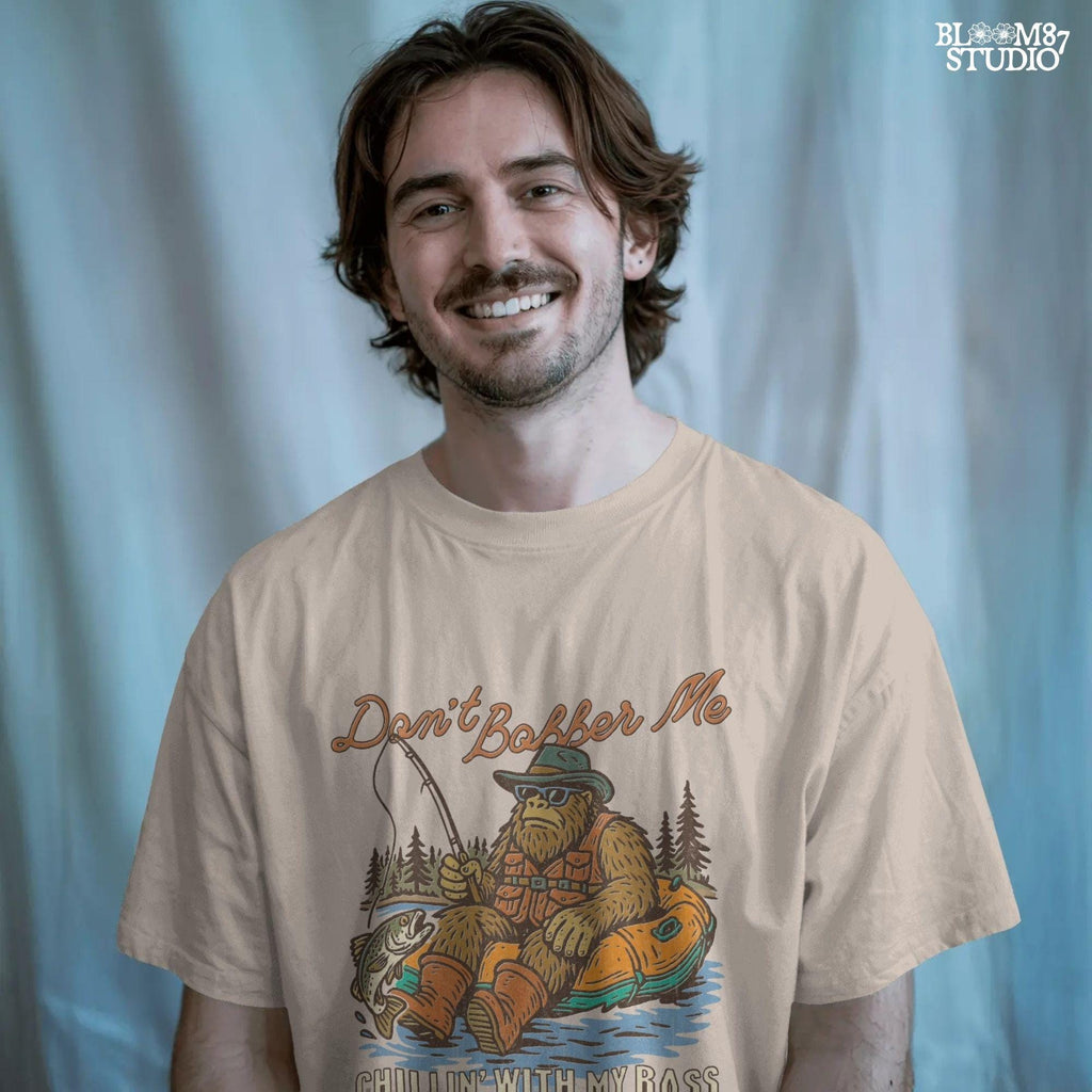 Funny Bigfoot sitting in a float tube holding a fishing rod and bass fish, wearing sunglasses and vest, with text “Don’t Bobber Me – Chillin’ with My Bass.”