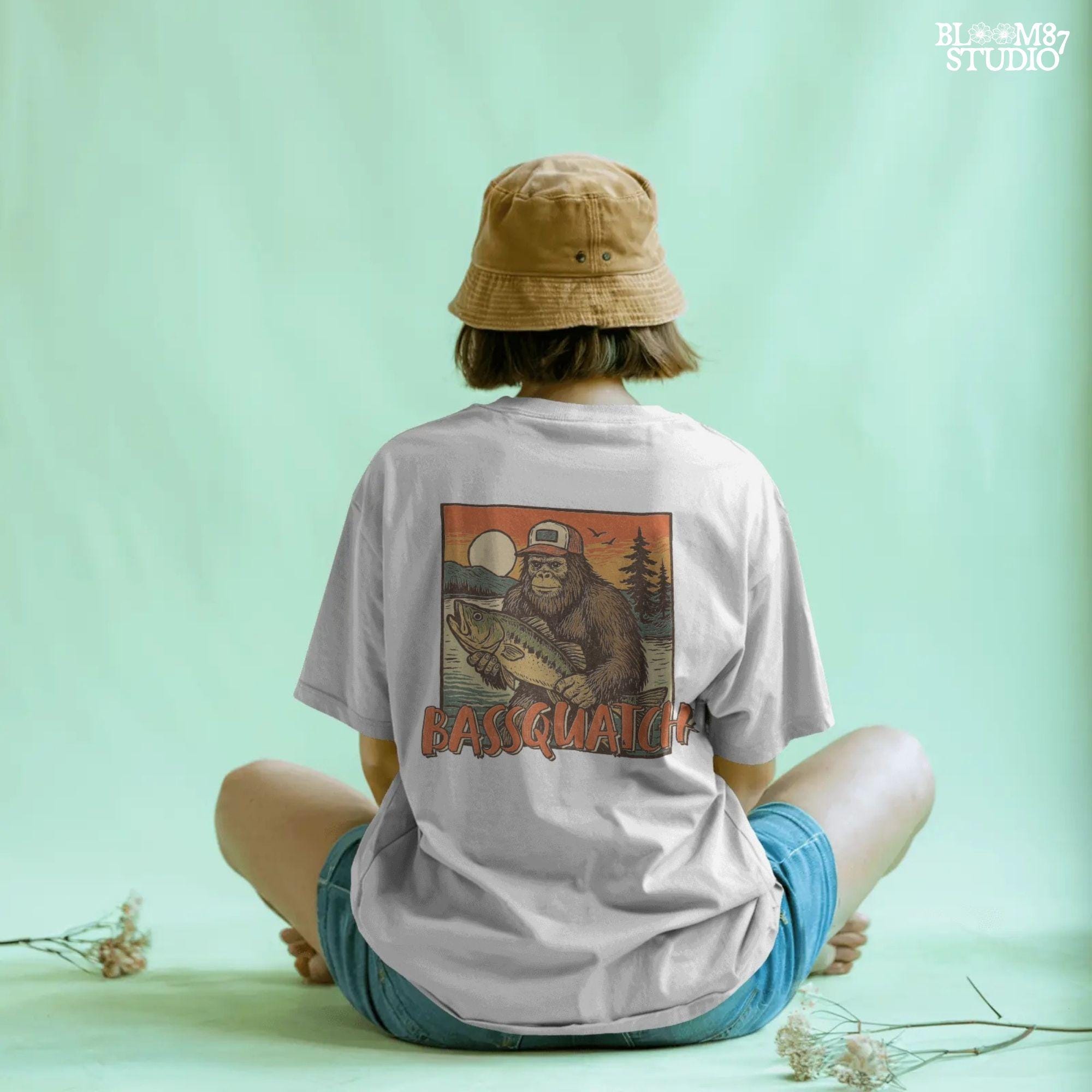 Bigfoot holding a large bass at sunset with summer lake background and the word “Bassquatch” in bold orange letters.