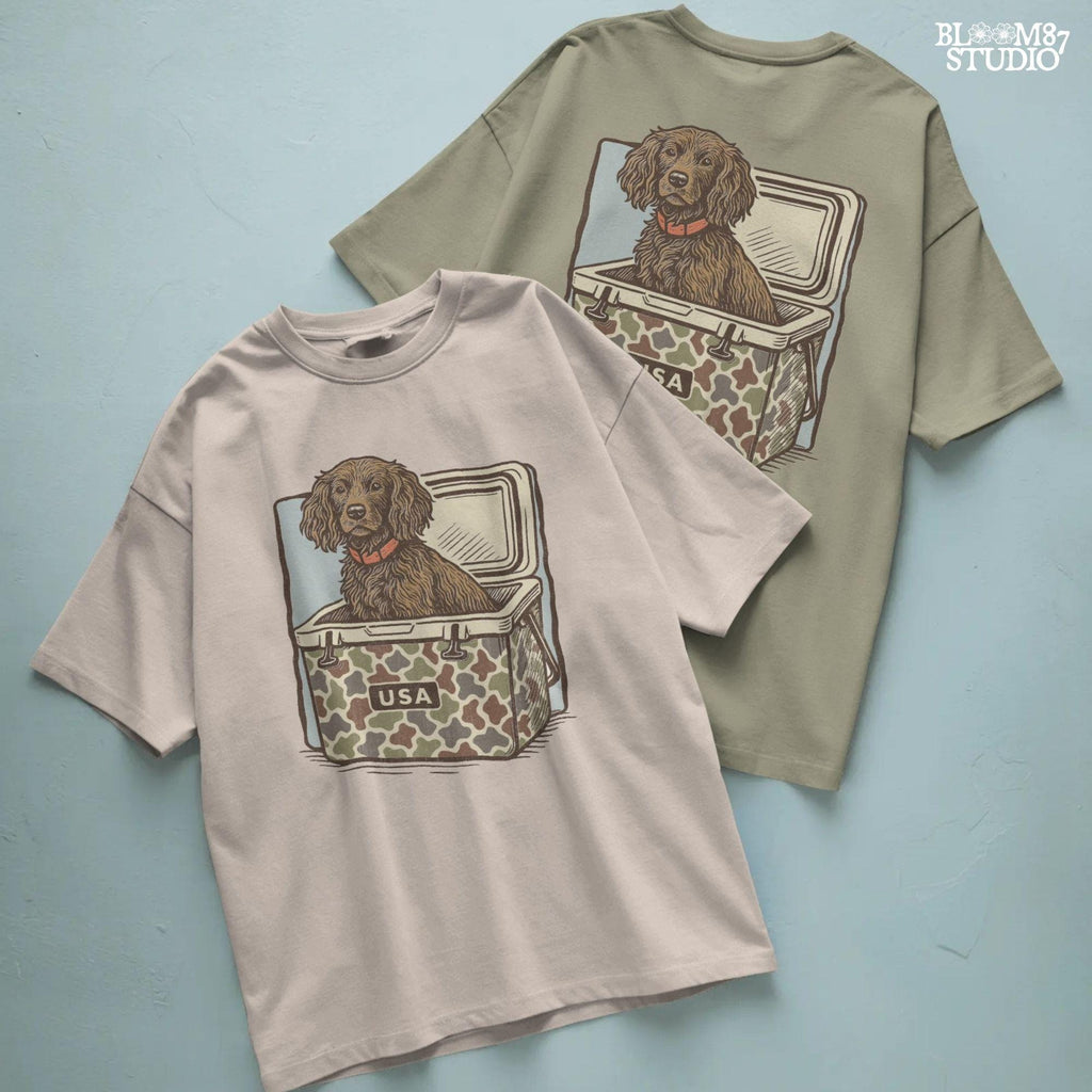 Hunting dog with curly fur sitting inside a camouflage cooler marked “USA” in a retro-style outdoors graphic.