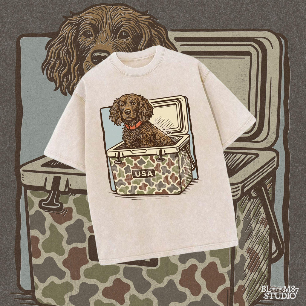 Hunting dog with curly fur sitting inside a camouflage cooler marked “USA” in a retro-style outdoors graphic.