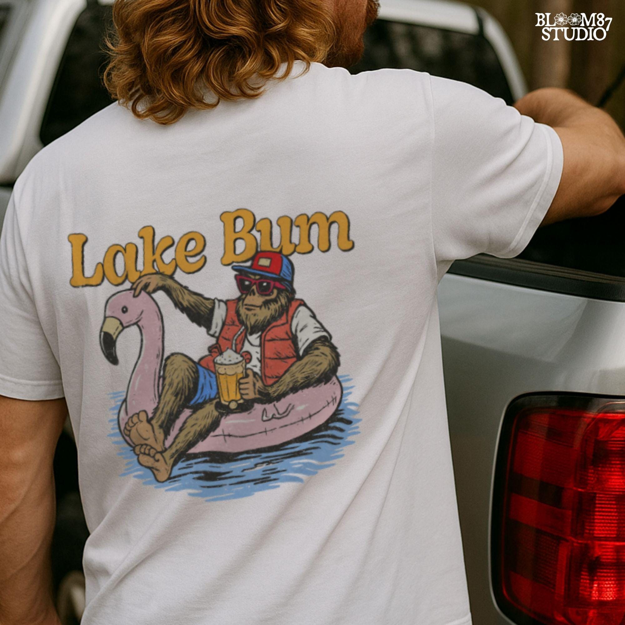Bigfoot lounging on a pink flamingo float with a beer, wearing summer gear and sunglasses, with “Lake Bum” text above.