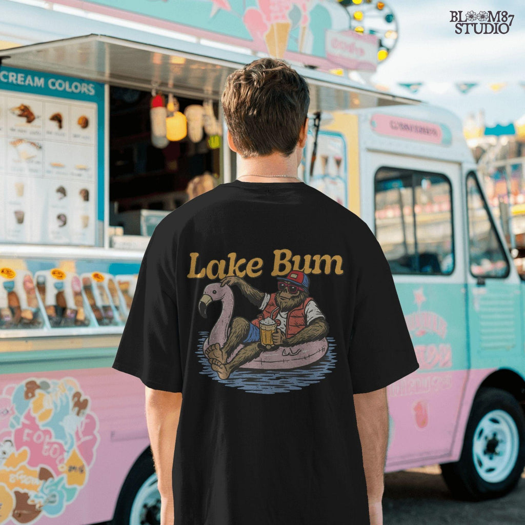 Bigfoot lounging on a pink flamingo float with a beer, wearing summer gear and sunglasses, with “Lake Bum” text above.