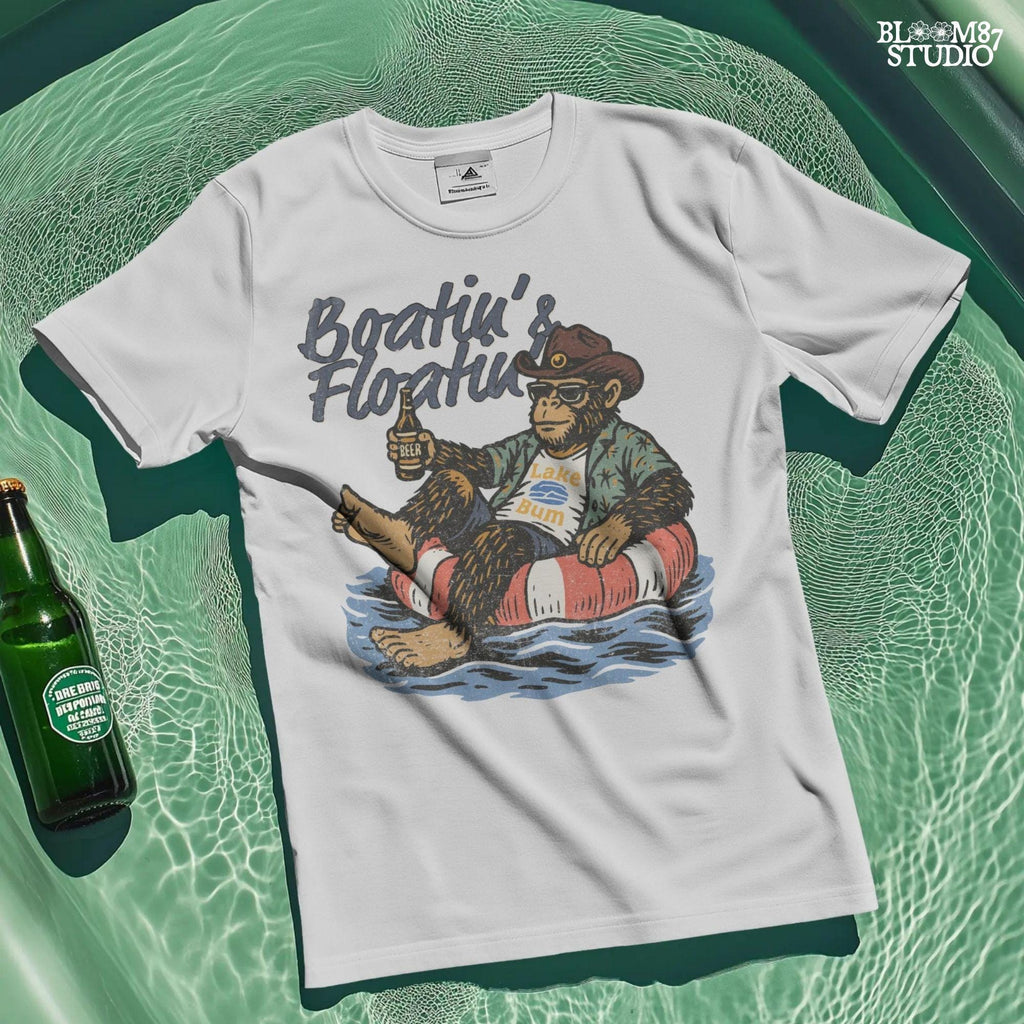 Bigfoot relaxing in a red and white pool float, holding a beer and wearing sunglasses, a hat, and a tropical shirt with “Boatin’ & Floatin’” text above.