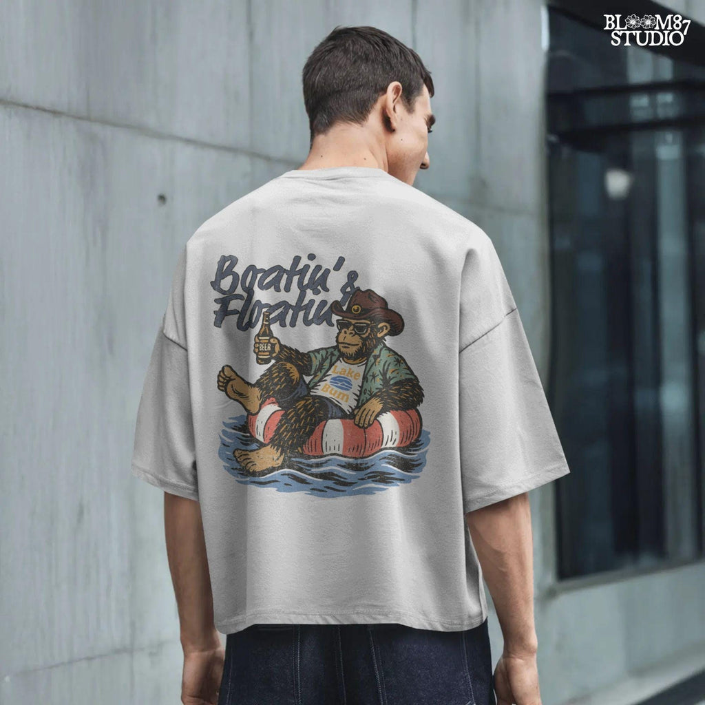 Bigfoot relaxing in a red and white pool float, holding a beer and wearing sunglasses, a hat, and a tropical shirt with “Boatin’ & Floatin’” text above.