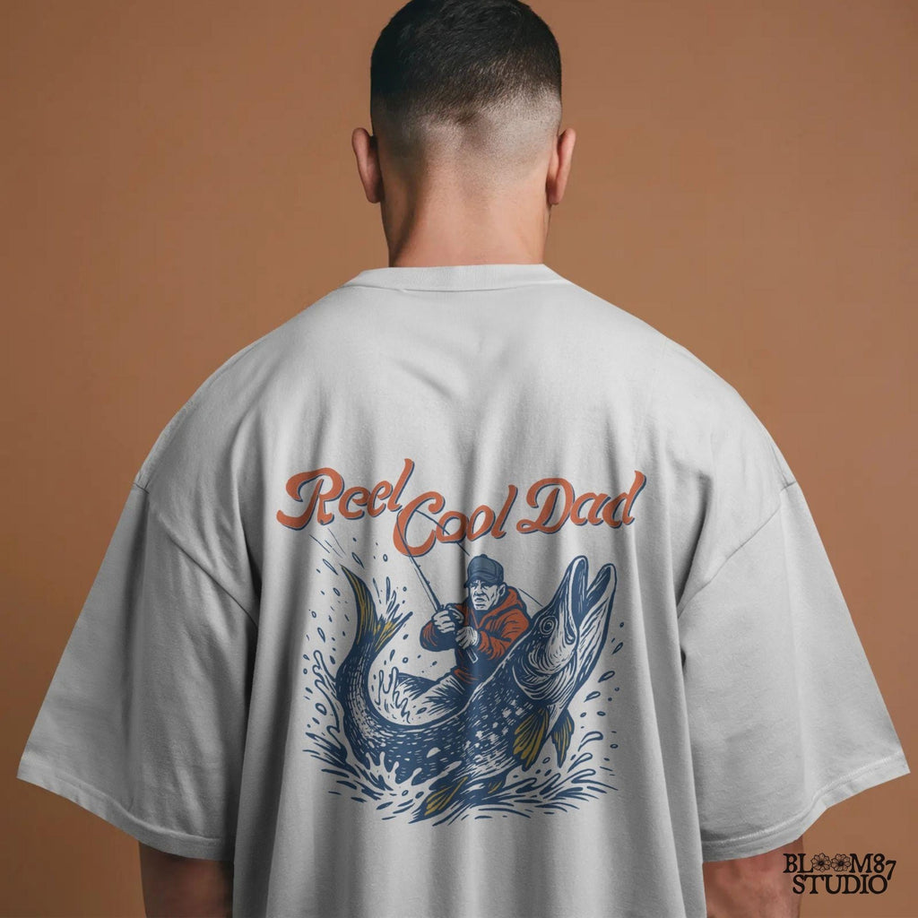 Illustration of a father reeling in a giant fish with bold text “Reel Cool Dad,” perfect for Father’s Day or fishing-themed gifts.