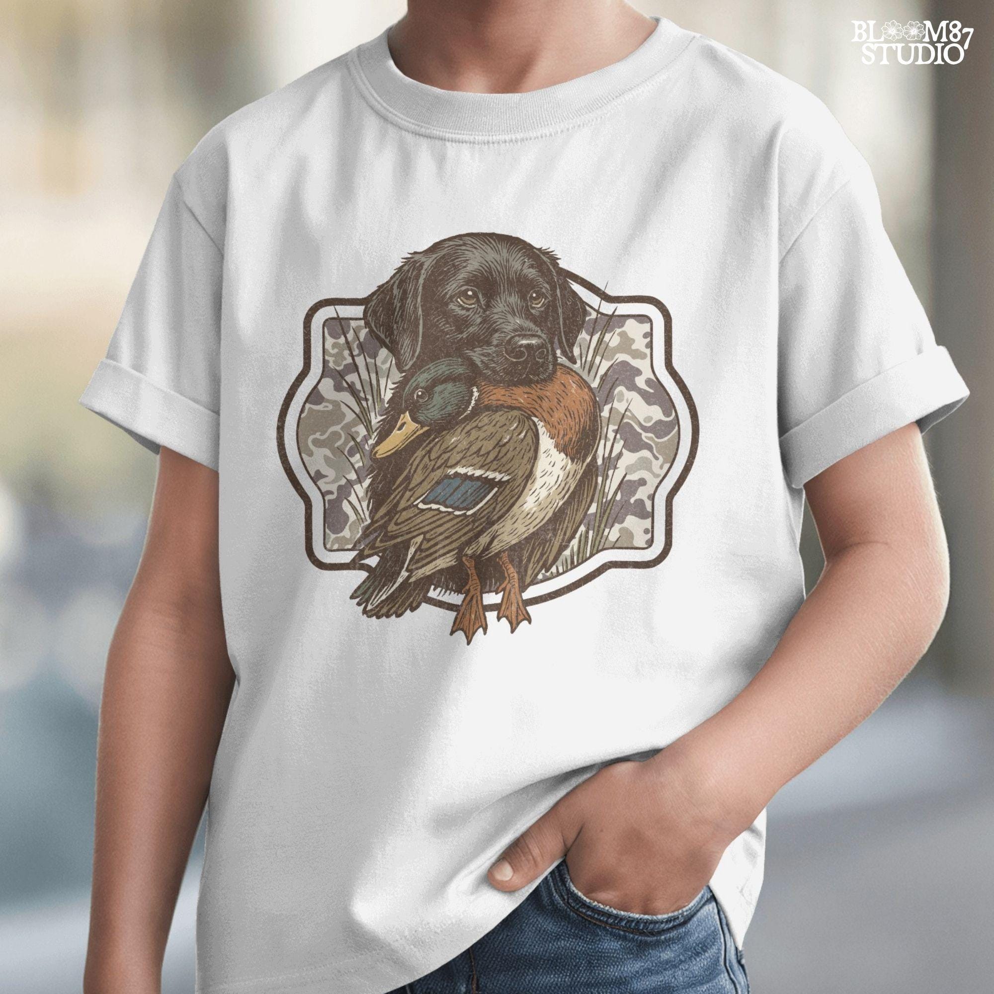 Black Labrador retriever holding a mallard duck with a camouflage background, perfect for hunting or outdoors-themed designs.