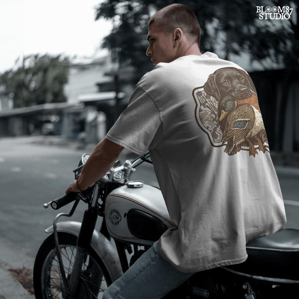 Black Labrador retriever holding a mallard duck with a camouflage background, perfect for hunting or outdoors-themed designs.