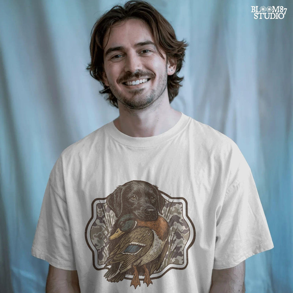 Black Labrador retriever holding a mallard duck with a camouflage background, perfect for hunting or outdoors-themed designs.