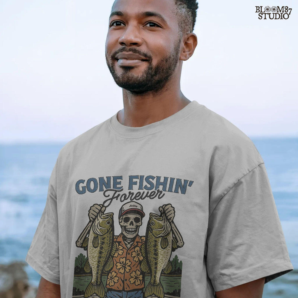 A skeleton wearing a red cap and orange floral shirt stands on a dock holding two large bass fish with the words “Gone Fishin’ Forever” above.