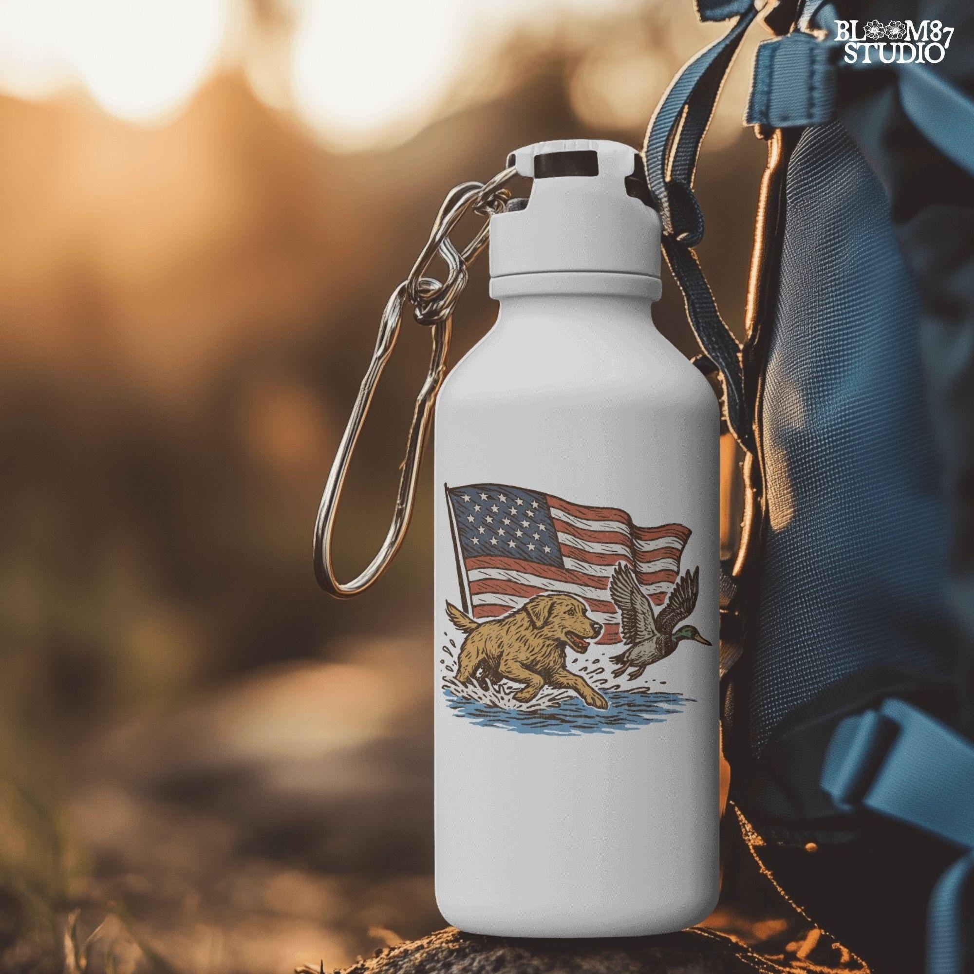 A yellow Labrador retriever splashing in water next to a flying duck, with a waving American flag in the background.