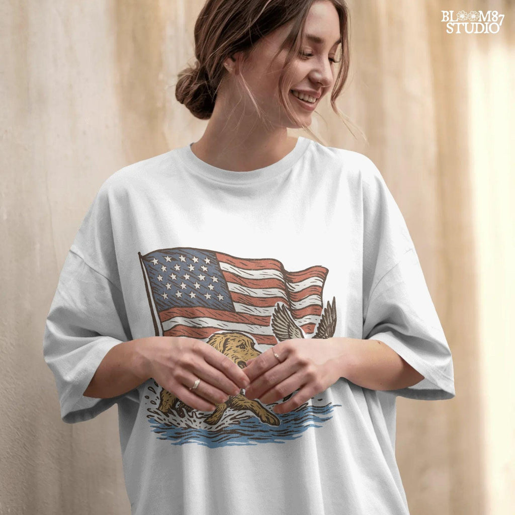 A yellow Labrador retriever splashing in water next to a flying duck, with a waving American flag in the background.