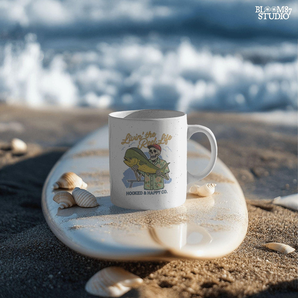 Cartoon skeleton in tropical shirt holding a mahi-mahi fish with text “Livin’ the Reel Life” above and “Hooked & Happy Co.” below.