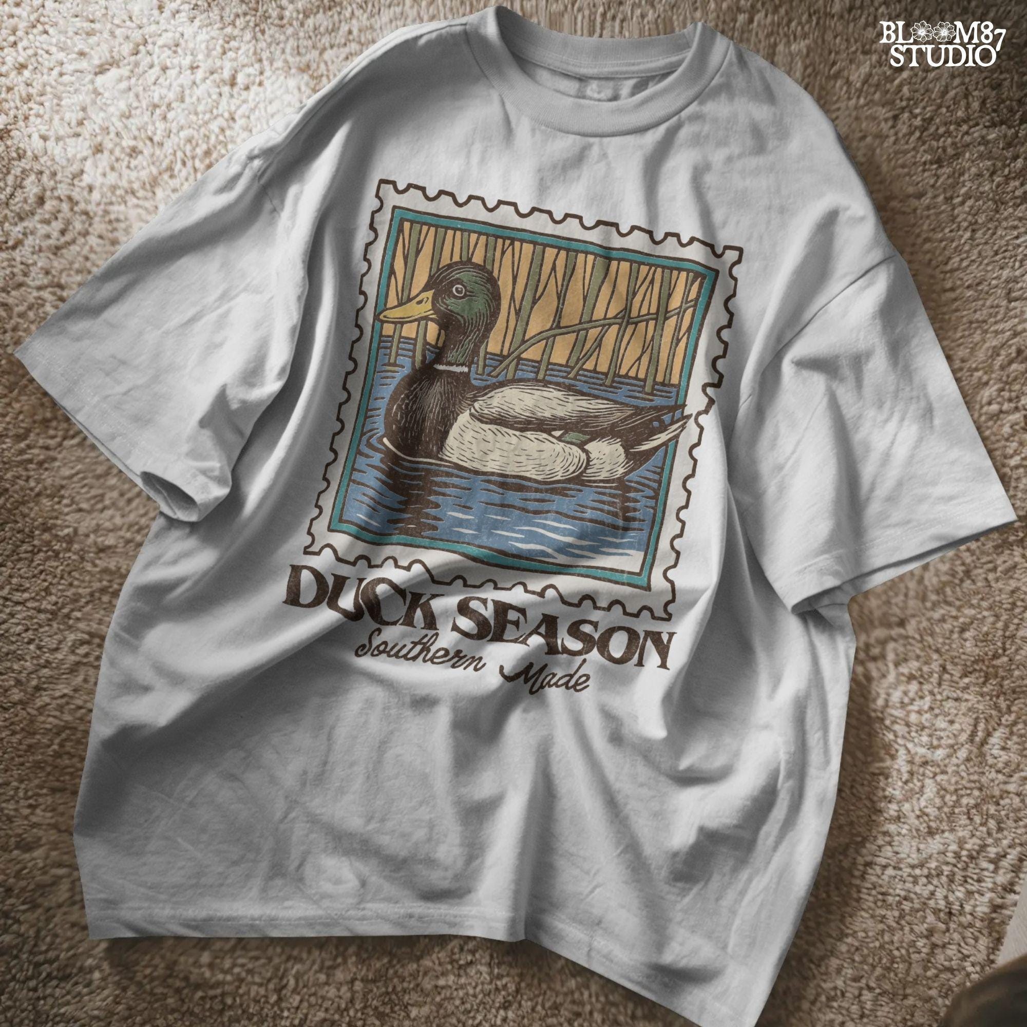 Vintage stamp-style mallard duck floating in water with forest background and text “Duck Season – Southern Made” in retro serif font.