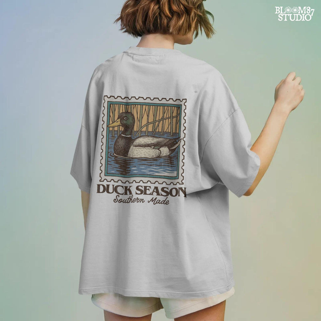 Vintage stamp-style mallard duck floating in water with forest background and text “Duck Season – Southern Made” in retro serif font.