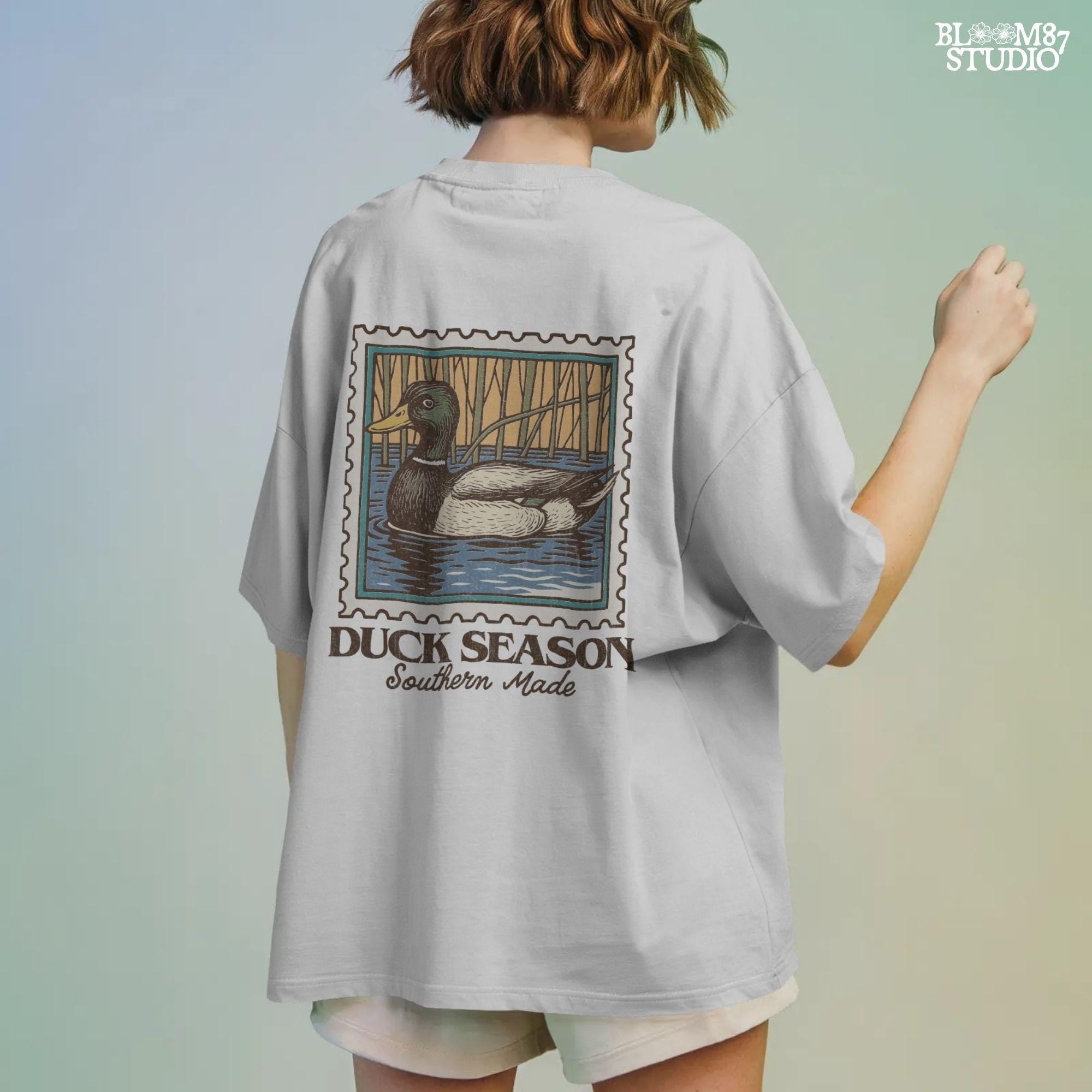 Vintage stamp-style mallard duck floating in water with forest background and text “Duck Season – Southern Made” in retro serif font.